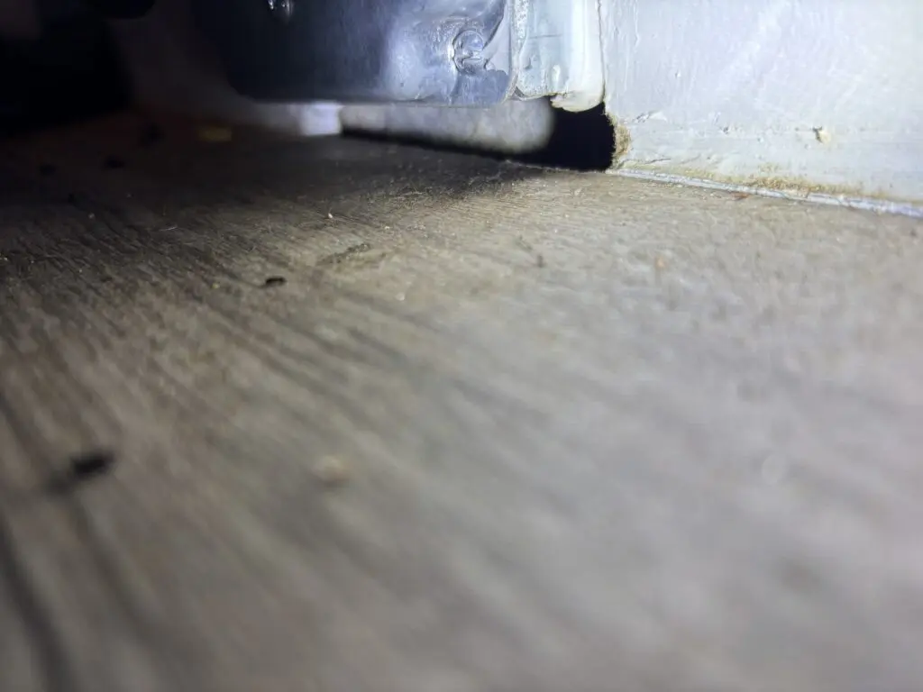 Black grease marks and rodent rub marks along baseboard near wall gap indicating active mouse or rat activity
